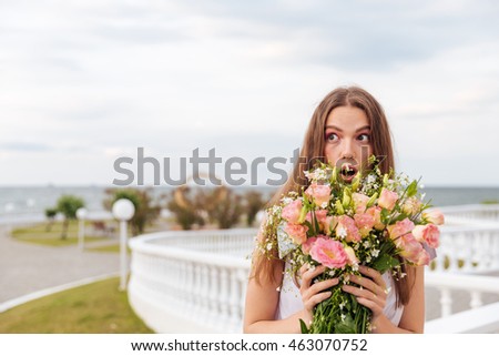 Portrait of a surprised young beautiful woman holding flowers outdoors