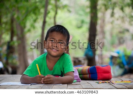 Asian cute little boy(poor kids) is drawing,painting with color pencil and study at old home.Homeless poor children,smile,lying on dirty wooden table and writing or coloring picture on books.