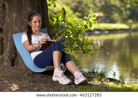 Young beautiful  pregnant  woman with book sits in the park.