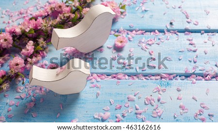 Two white wooden decorative birds and pink  sakura flowers  on blue wooden planks. Selective focus. Place for text.  Toned image.