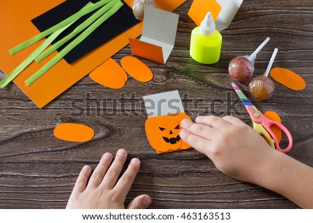 The child create a greeting packaging for lollipop on Halloween pumpkin paper, be glued for paper the details. Children's art project, a craft for children.