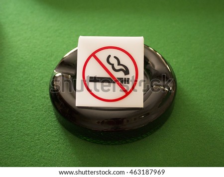 A bright photograph of a public domain no smoking sign / icon on a deep bottle green ashtray with a green felt background - with a slight grainy finish on lesser objects (for main object emphasis)