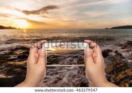Hand of photographer using smart phone mobile shooting image on seascape in twilight,  Photographer holding mobile smart phone with photograph and photography
