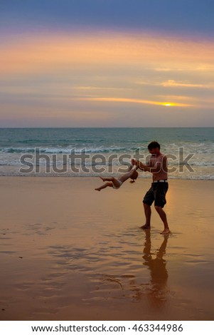 Father plays with his daughter at the beach near the sea at the spectacular cloudy sunset
