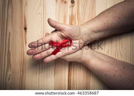 Hands of elderly woman and an international symbol of the fight against breast cancer on light wooden background. Toned.
