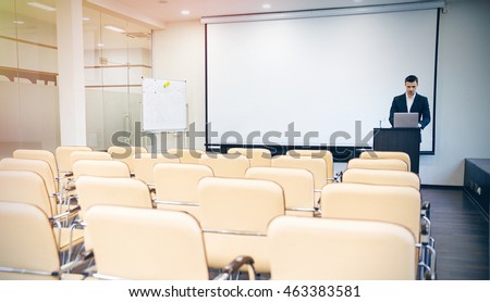 Serious handsome speaker preparing for the conference using laptop in empty boardroom Royalty-Free Stock Photo #463383581