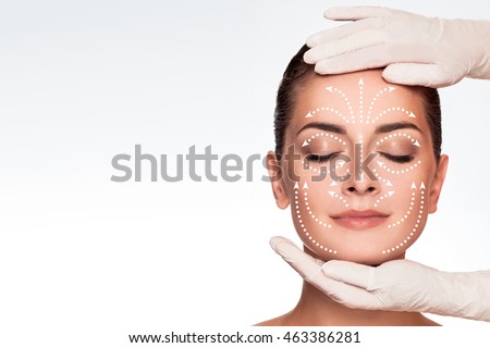 Young attractive woman getting spa treatment. Beautiful girl receiving massage face. Anti aging treatment and plastic surgery concept. Eyes closed with serene expression and white arrows over face Royalty-Free Stock Photo #463386281