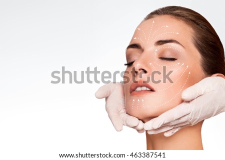 Young attractive woman getting spa treatment. Beautiful girl receiving massage face. Anti aging treatment and plastic surgery concept. Eyes closed with serene expression and white arrows over face Royalty-Free Stock Photo #463387541