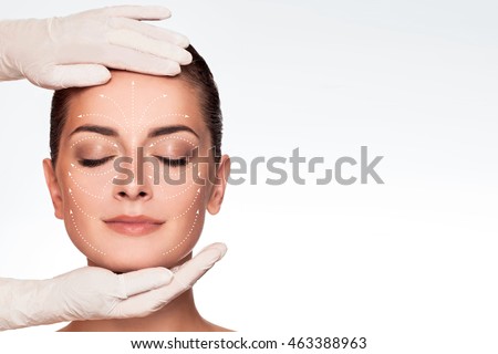 Young attractive woman getting spa treatment. Beautiful girl receiving massage face. Anti aging treatment and plastic surgery concept. Eyes closed with serene expression and white arrows over face Royalty-Free Stock Photo #463388963