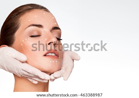 Young attractive woman getting spa treatment. Beautiful girl receiving massage face. Anti aging treatment and plastic surgery concept. Eyes closed with serene expression and white arrows over face Royalty-Free Stock Photo #463388987