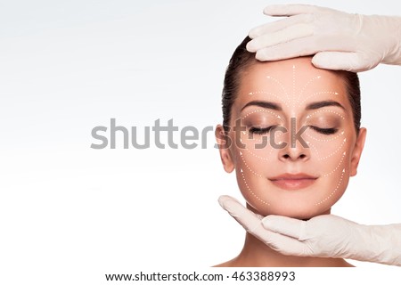 Young attractive woman getting spa treatment. Beautiful girl receiving massage face. Anti aging treatment and plastic surgery concept. Eyes closed with serene expression and white arrows over face Royalty-Free Stock Photo #463388993