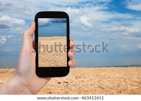 travel concept - tourist photographs of shelly and sand beach of Azov Sea on smartphone