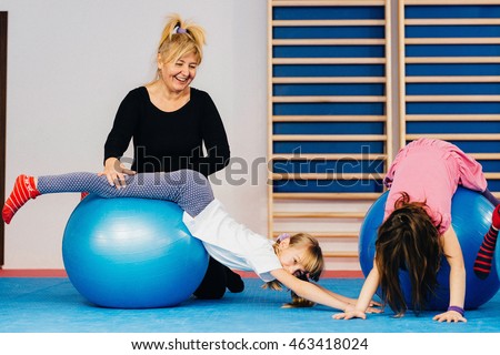 Physical therapist working with little girls in school gymnasium, exercising with fitness ball
