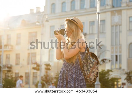 portrait of pretty young woman having fun in the city in Europe in evening with camera. travel photo of photographer Making pictures in hipster style glasses and hat.