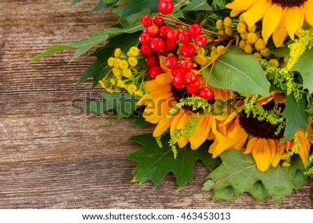 Bunch of fresh sunflowers with green leaves and red berries on wood close up