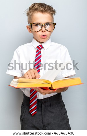 Back to school concept. Cheerful smiling little boy holding book on a grey background