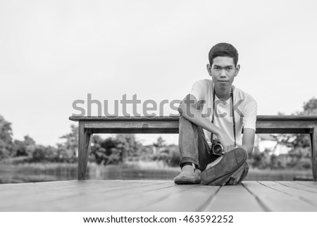 Young photographer sitting on the wooden deck beside the water with sunrise.?Black white tone.
