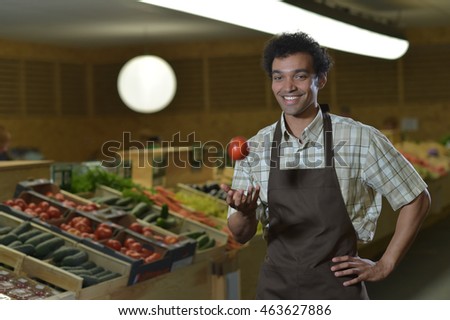 Young Grocery clerk juggling with tomatoes in produce aisle of grocery store