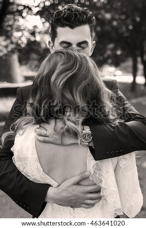 Black and white picture of a handsome man closing her eyes while hugging curly woman