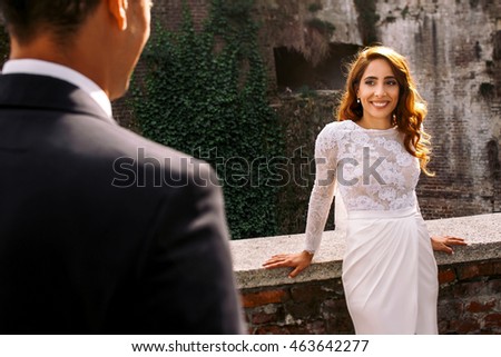 Sun illuminates bride's golden curls while she leans on the wall waiting for a groom