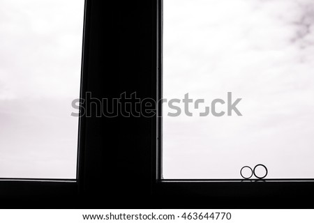 Black and white picture of wedding rings standing on the window frame and white sky outside