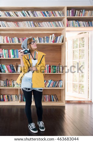 woman standing in library and holding camera,woman in yellow jacket, Smiling Asian woman holding camera and posing for camera