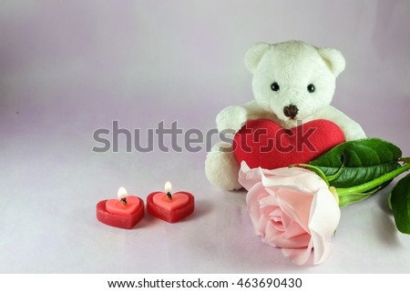 Lovely white teddy bear decorated with red heart, heart shape candles and pink rose.
