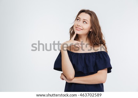 Smiling pensive young woman standing and dreaming over white background