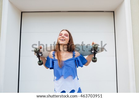 Laughing young girl standing with skateboard outdoors over white wall background