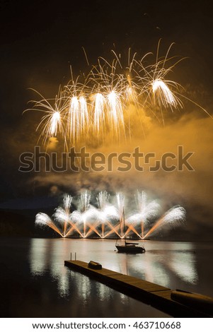 Ignis Brunensis yellow silver gold colored firework resembling aster flower reflecting on dam water surface. Long exposure night graphical photography using creative tilt effect by tilt-shift lens.