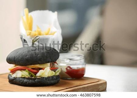 Tasty black burger with french fries and sauce on wooden cutting board