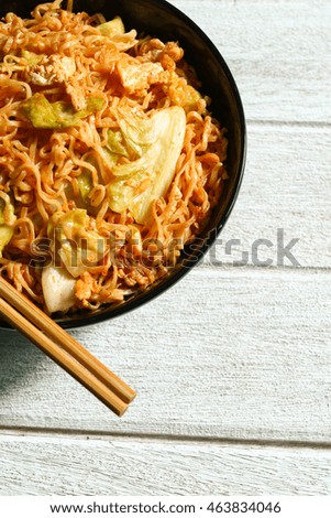 Instant noodles, fried pork, and lettuce in black cup and chopsticks on white table