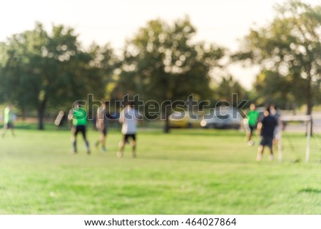 Blurred abstract motion group of young African American and Asian people playing football on green soccer pitch of the park at sunset with warm light at Houston, Texas. Urban healthy lifestyle concept