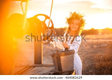 Very beautiful young girl in the embroidered shirt and a wreath on the head of field herbs in the village at sunset. Ukraine.