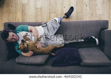 Quadruple amputee relaxing on the sofa at home with his dog.  Royalty-Free Stock Photo #464102141