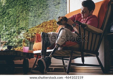 Quadriplegic man and his dog having quality time on the sofa at home. The dog is lying on the mans amputated legs. Royalty-Free Stock Photo #464102159