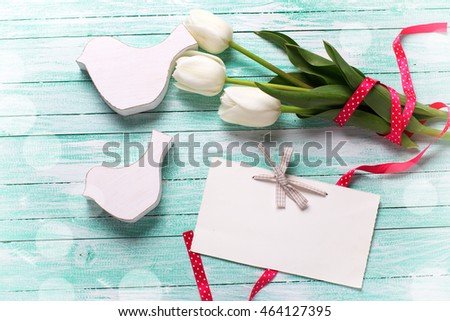 White tulips flowers, empty tag and  two decorative birds  on turquoise wooden background. Selective focus. Place for text. Flat lay. Toned image.