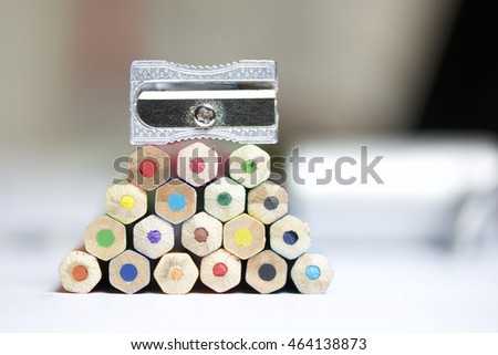 Colored pencils stacked pyramid. At the top of the pyramid set sharpener.