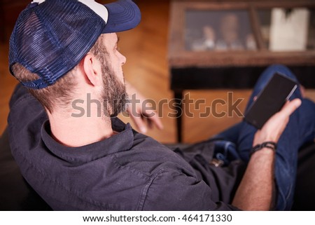 Man sitting on a couch in the living room with a mobile phone looking back
