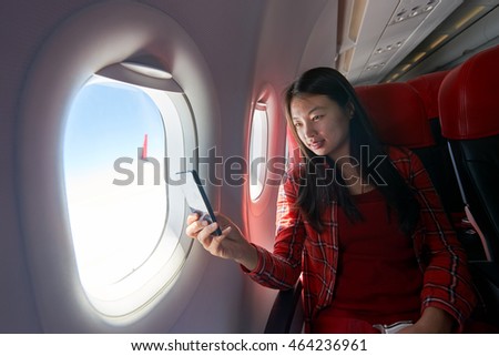 Young woman with smartphone inside of a single-aisle aircraft.
