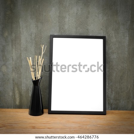 Frame black square on a white. And shaft wear in dry brownish black ceramic vase on a wooden table, brown, which is strong. The back wall is cement gray.