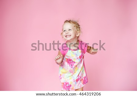 little happy girl in pink colored dress with blonde hair on pink background in Studio