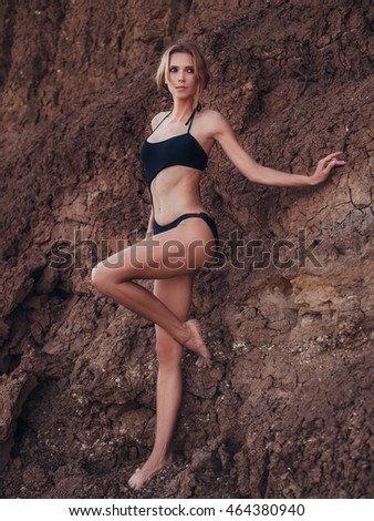 A beautiful slender girl is resting on the beach in a black bikini, blonde hair, blue eyes, fashion model