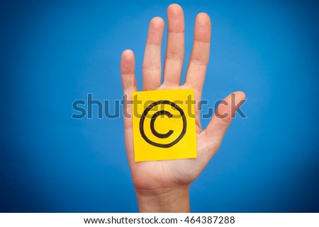 Yellow paper note with Copyright symbol in woman palm. Blue background.