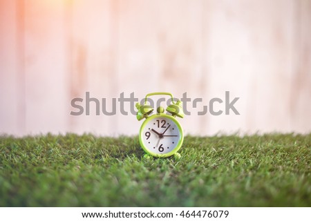 green little alarm clock on green grass texture floor time concept