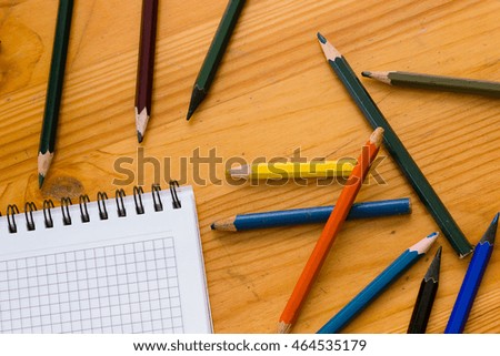 Variegated colored pencils and white square-lined paper notebook on a light orange wooden study table atop