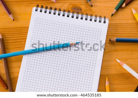 Variegated colored pencils and white square-lined paper notebook on a light orange wooden study table atop close-up