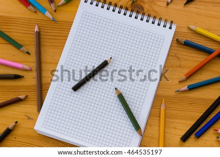 Variegated colored pencils and white square-lined paper notebook on a light orange wooden study table atop