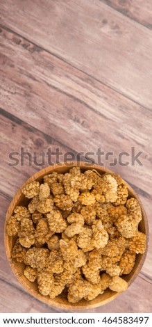 Dried white mulberries in wooden bowl over wooden background