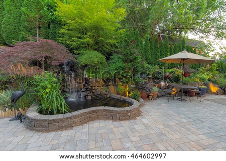 Backyard Garden landscaping with waterfall pond trees plants trellis decor furniture brick pavers patio hardscape Royalty-Free Stock Photo #464602997